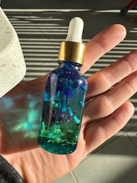 a hand holding a small bottle of blue and green liquid