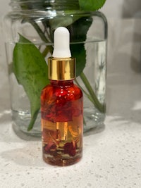 a small bottle of rose oil next to a glass of water